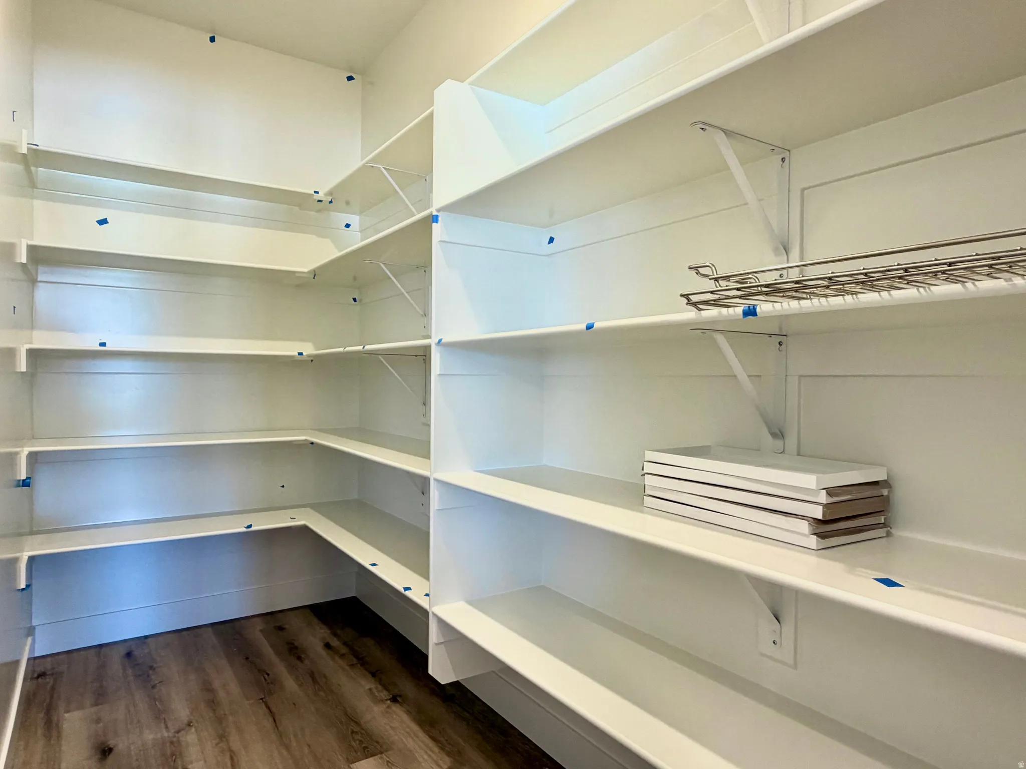 Spacious pantry featuring extensive white shelving, wood-finish flooring, and a wire rack system for versatile organization
