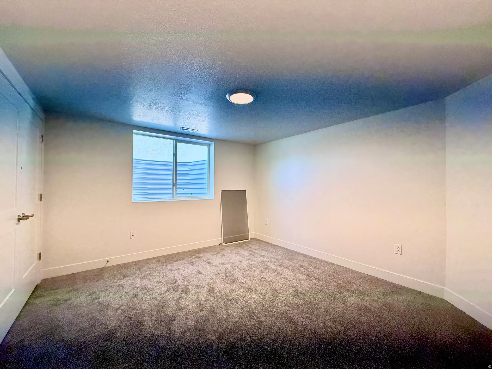 Carpeted room featuring a white door with brushed nickel hardware, a flush mount ceiling light, a window with horizontal blinds, and white baseboards