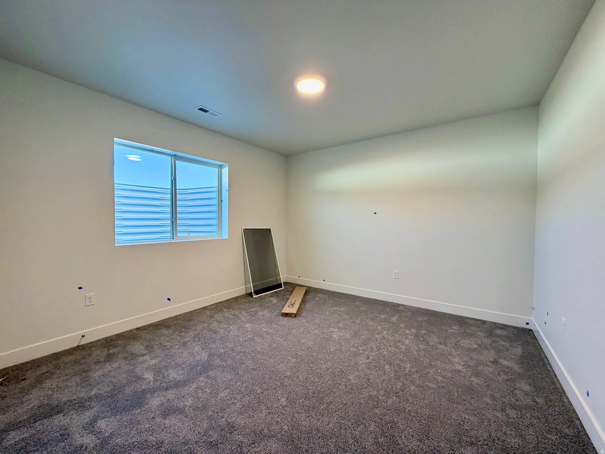 Windowed room featuring plush gray carpeting, white painted walls, white baseboards, and a recessed ceiling light fixture