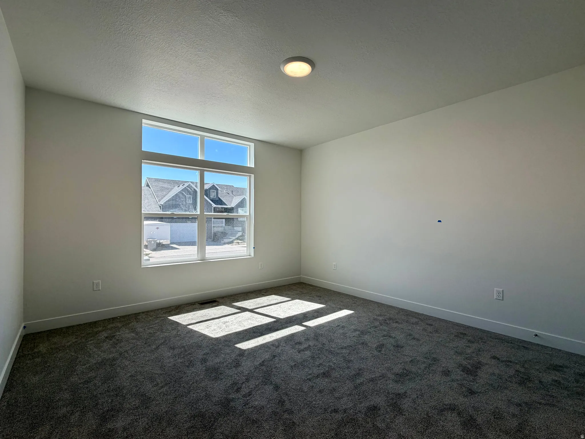 Spacious room featuring a large window with transom, neutral wall color, contemporary ceiling light fixture, and dark gray carpeting