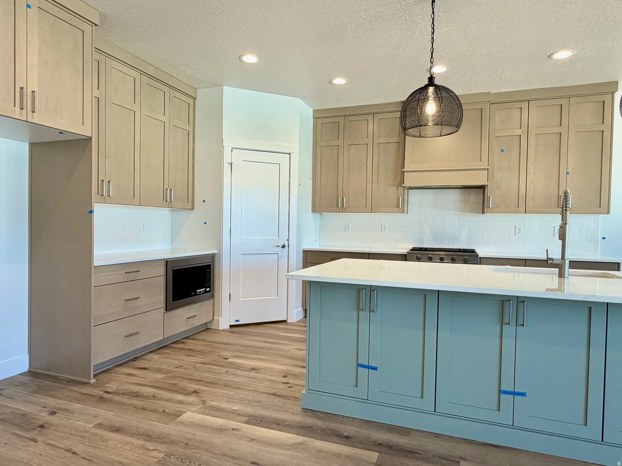 Modern kitchen featuring a light wood-finish flooring, a two-toned cabinetry scheme with a prominent light blue island, white countertops, and a white subway tile backsplash