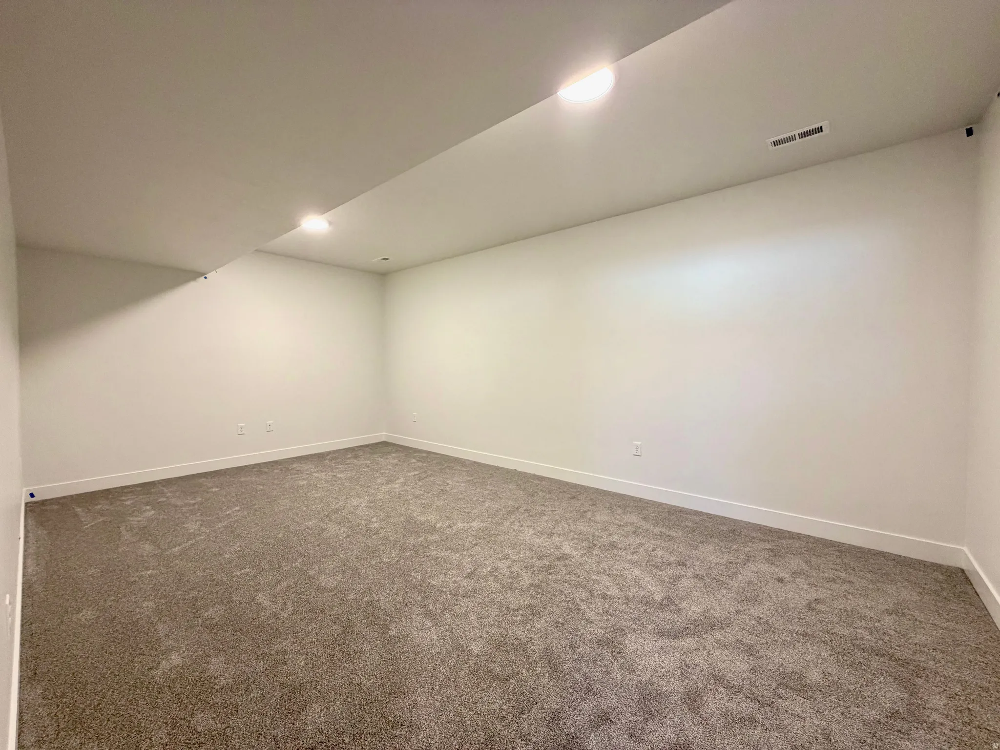 Spacious room with new carpet flooring, crisp white walls, recessed lighting, and white baseboards