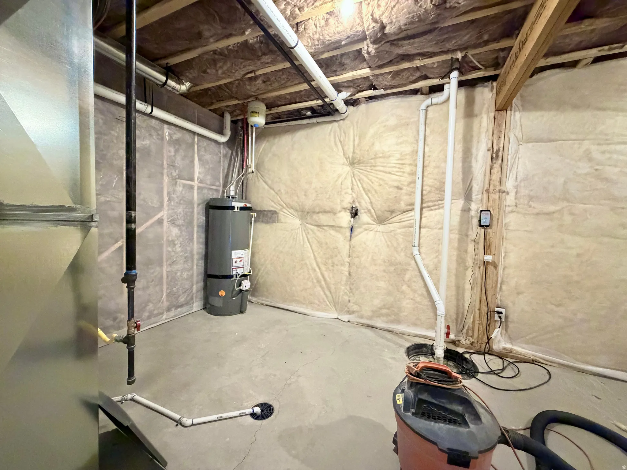 Basement utility area featuring a water heater, exposed ductwork, pipework, and insulated walls