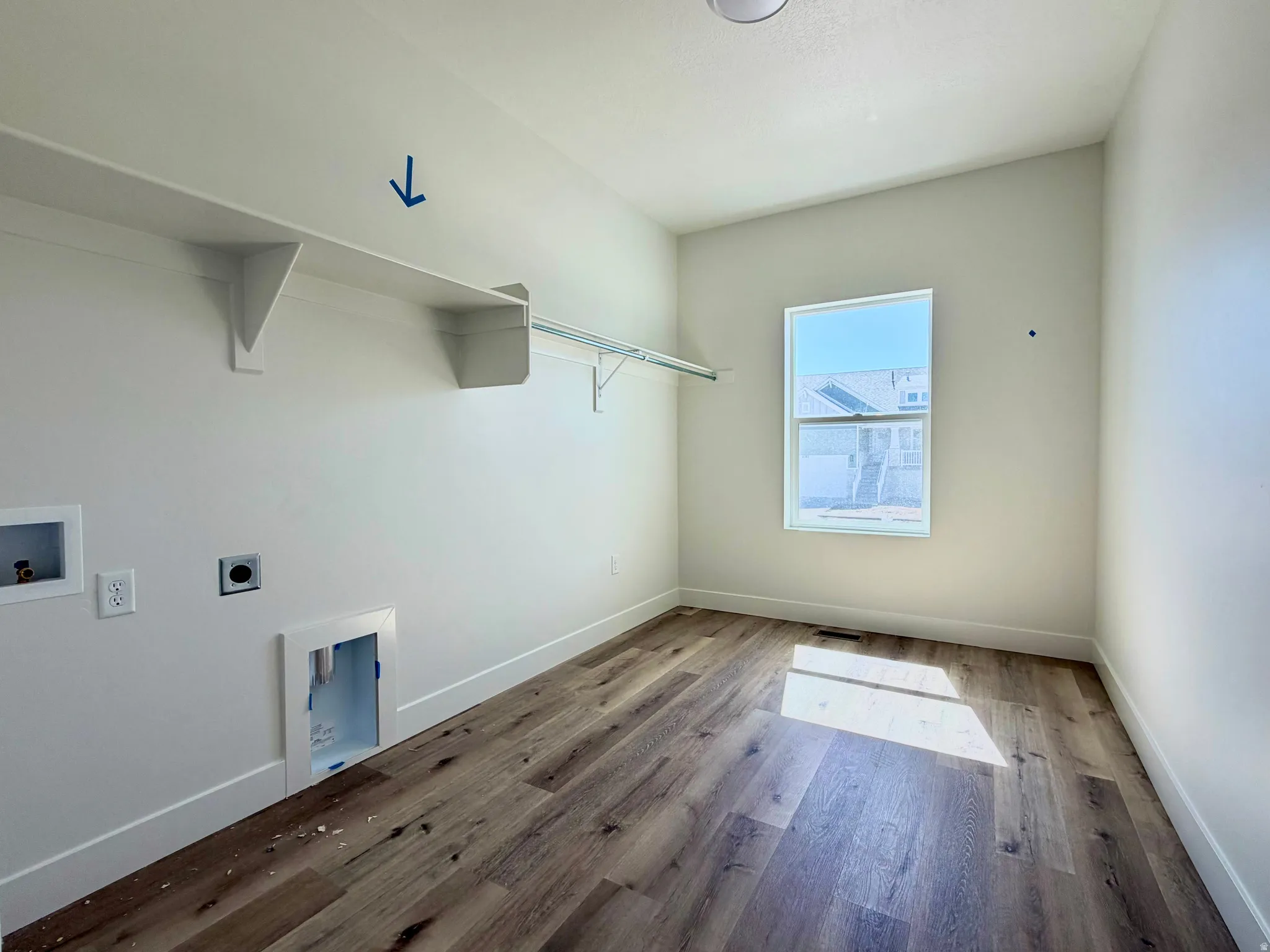 Dedicated laundry space featuring wood-finish flooring, a single window, built-in shelving, and a hanging rod