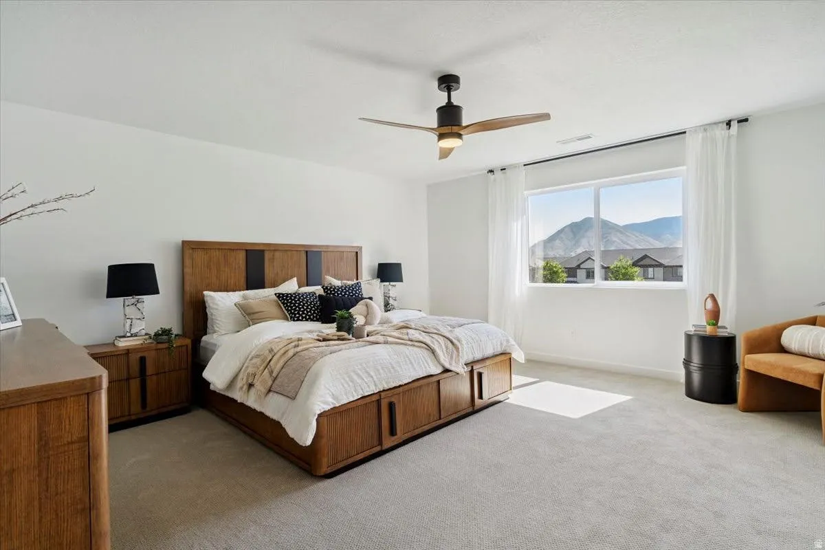 Carpeted bedroom featuring a large picture window with mountain scenery, a ceiling fan with integrated lighting, and white window treatments