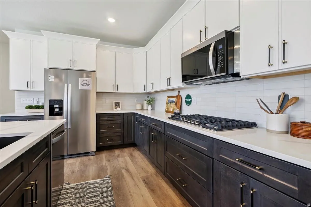 Modern kitchen featuring two-tone cabinetry with white upper cabinets and dark lower cabinets, light-toned countertops, a stainless steel side-by-side refrigerator, a built-in microwave, and a gas range