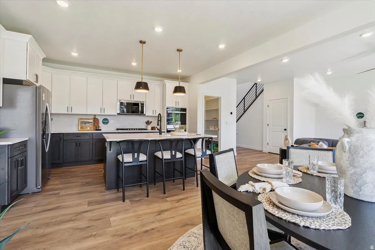 Open-concept kitchen and dining area featuring wood-finish flooring, two-tone cabinetry with white upper and dark lower units, a central island with seating, stainless steel appliances, and recessed lighting