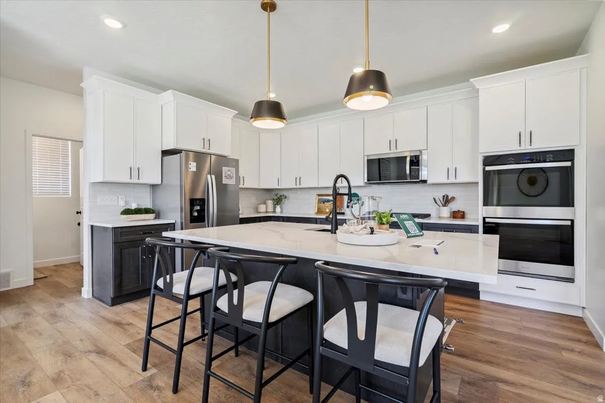 Modern kitchen featuring an expansive center island with seating, stainless steel appliances, and a built-in double oven
