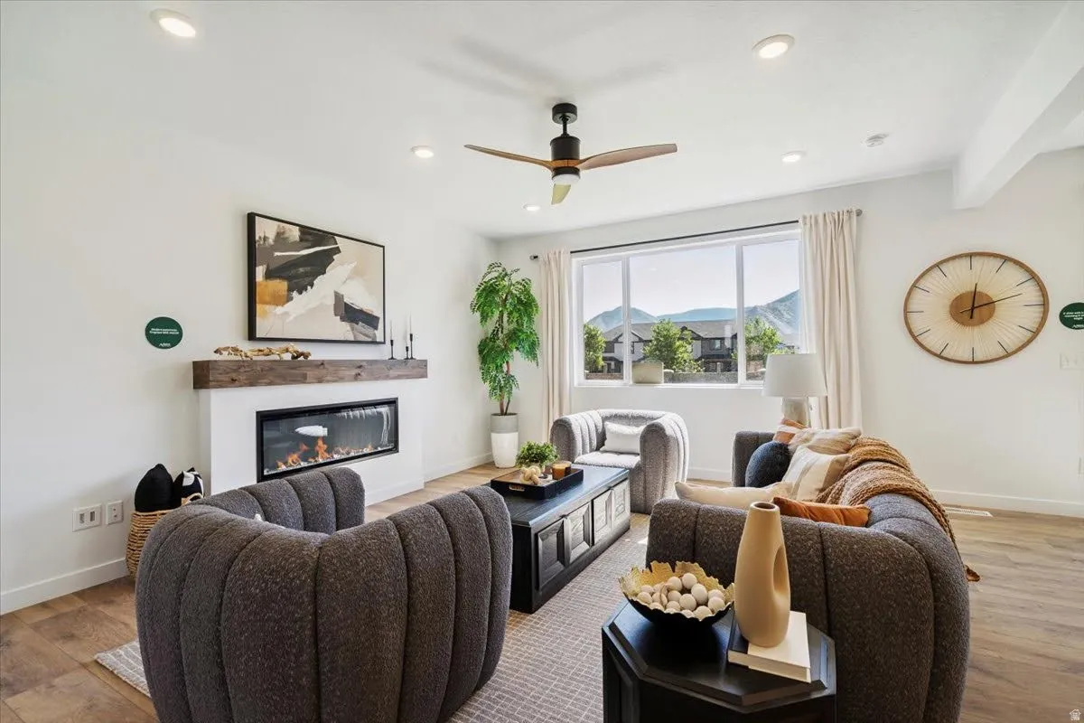 Living area featuring wood-finish flooring, a linear fireplace with a substantial wood mantel, recessed lighting, and a ceiling fan