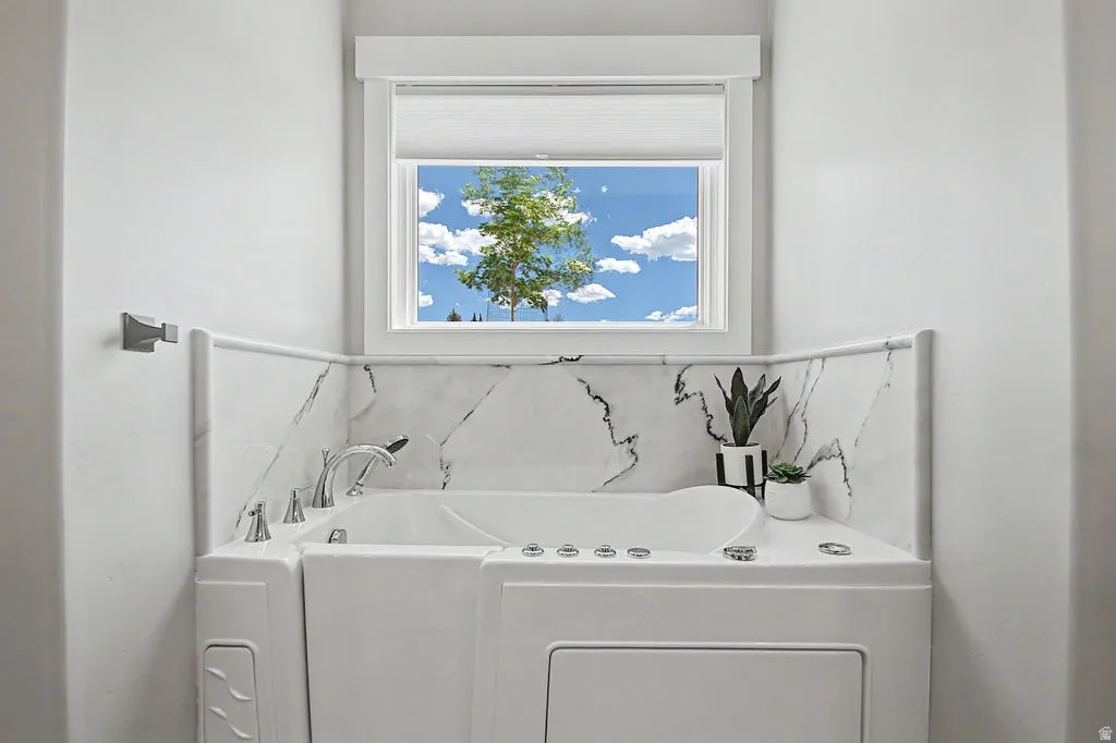Corner walk-in tub with chrome fixtures, surrounded by a white and grey veined tile backsplash
