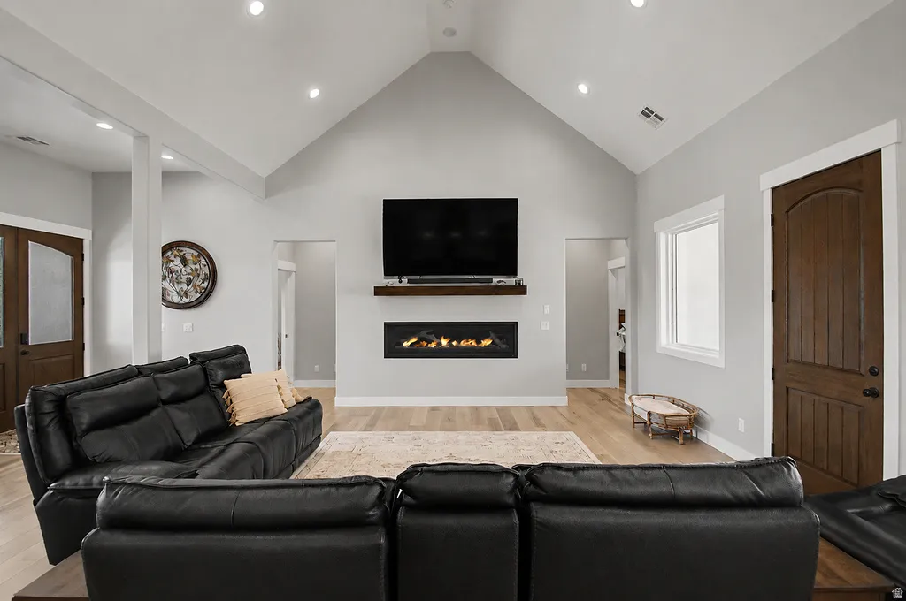 Vaulted ceiling living area featuring light wood-finish flooring, a contemporary linear fireplace with a floating mantel, recessed lighting, and a white-trimmed window