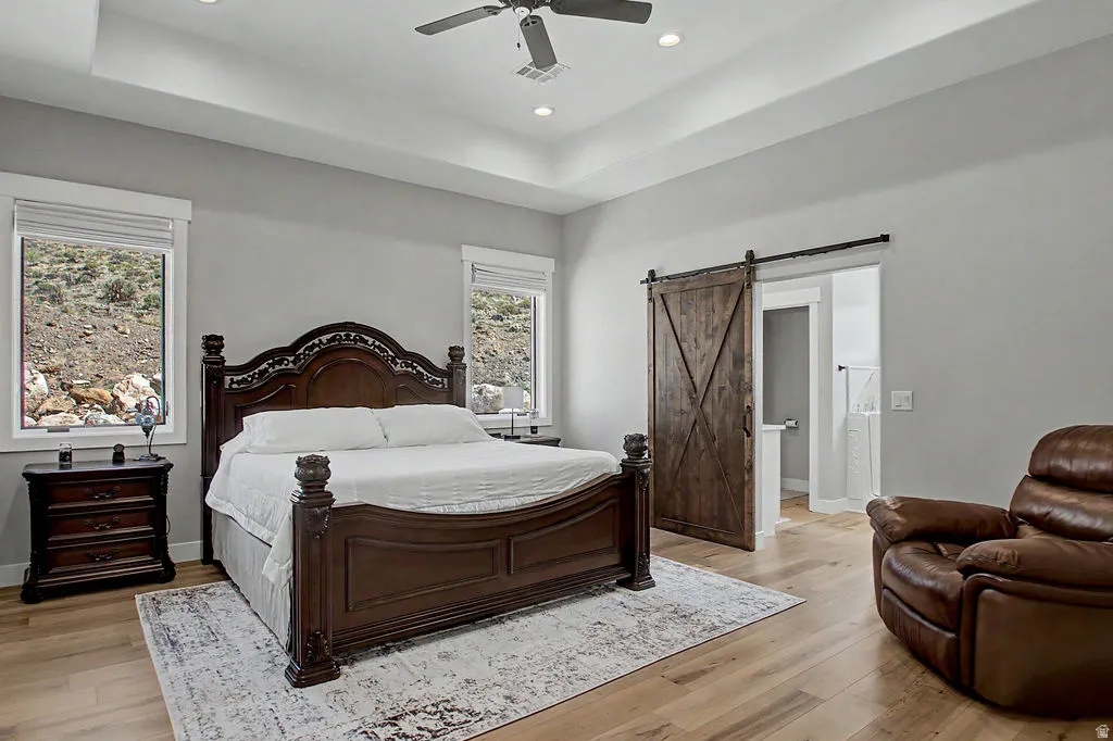 Spacious bedroom featuring light wood-finish flooring and a tray ceiling with recessed lighting