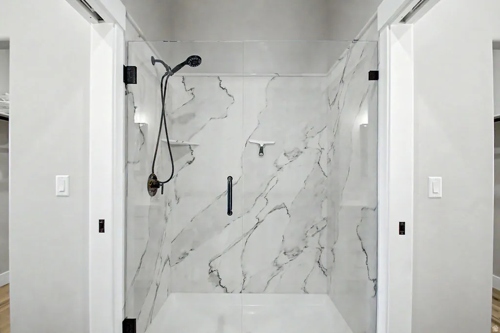 Walk-in shower featuring glass enclosure, marble-style wall panels, matte black shower fixtures, and integrated lighting