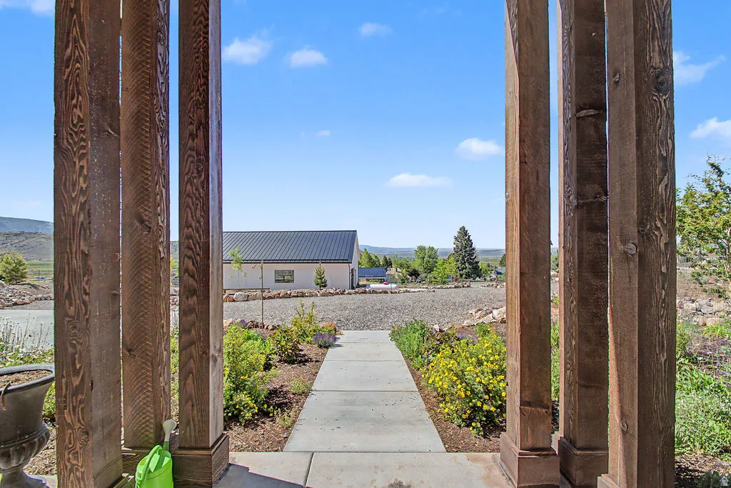 Expansive outdoor space featuring a concrete pathway, landscaped grounds with diverse plantings, and a distant building with a dark metal roof