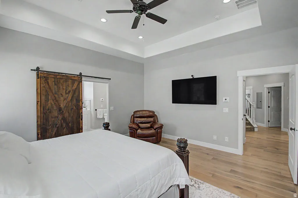 Spacious room featuring wood-finish flooring, a tray ceiling with recessed lighting, and a ceiling fan