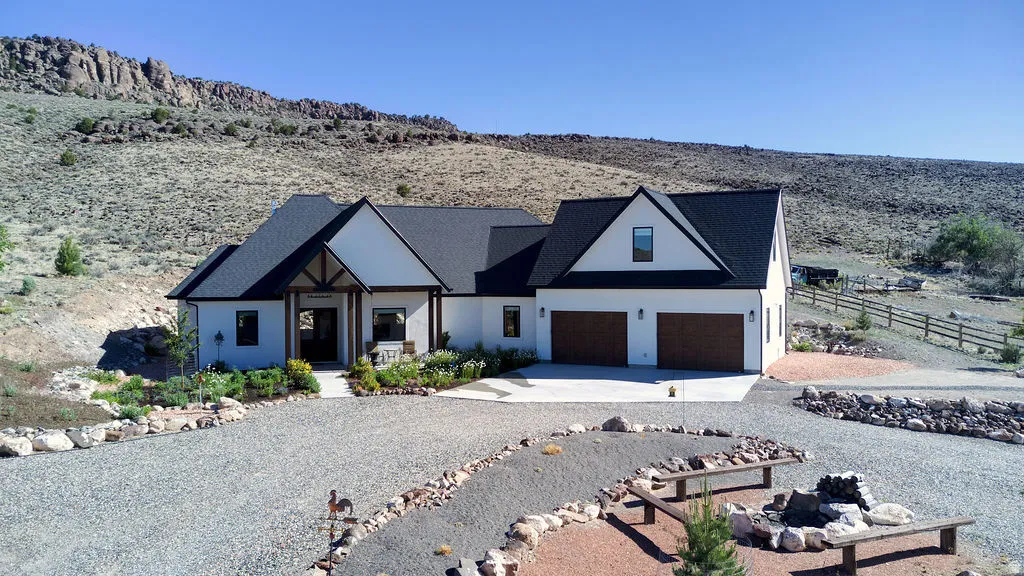 Contemporary residence featuring a white stucco exterior, black asphalt shingle roof, dark wood-finish garage doors, and a decorative wood-truss entry