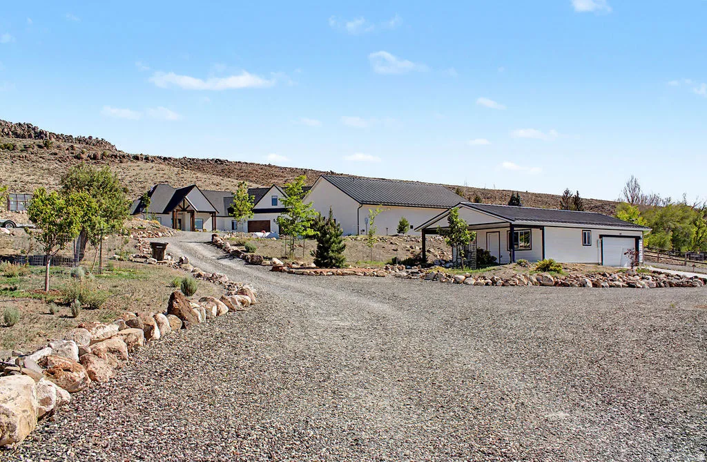 Gravel driveway with a stone border leading to multiple structures, including a white building with a dark roof and an attached covered porch
