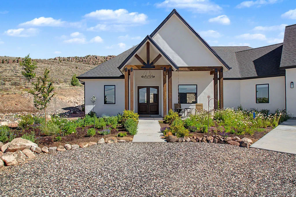 Contemporary stucco exterior featuring a gabled entryway with exposed wood beams, a dark-stained double entry door, and a covered porch area