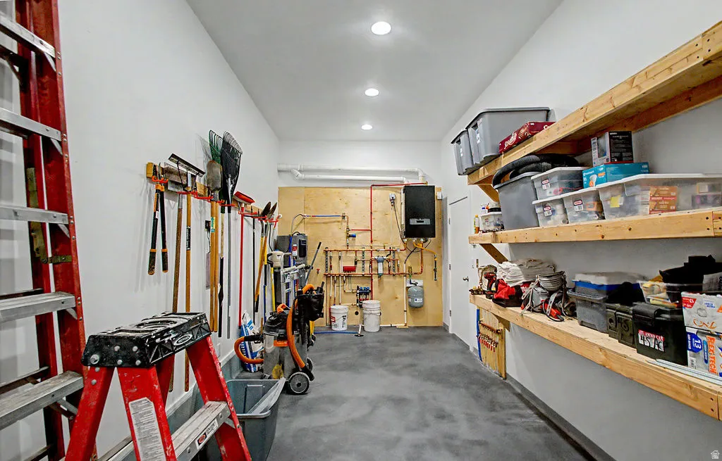 Utility room featuring built-in wooden shelving, a wall-mounted tool organization system, a tankless water heater, exposed copper piping, and recessed ceiling lighting