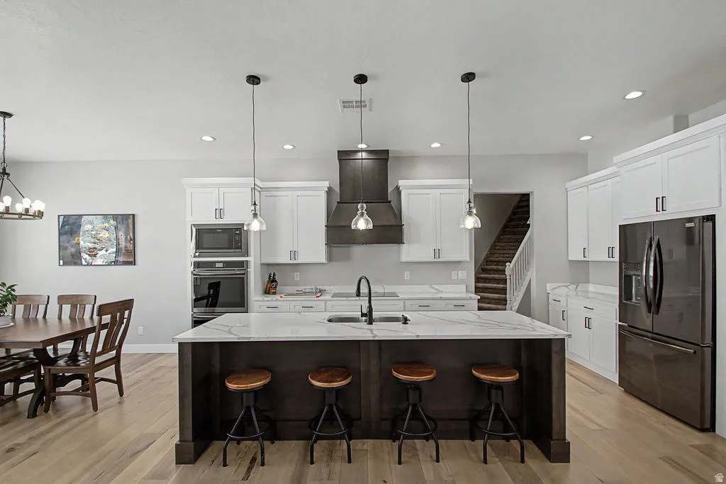 Open-concept kitchen featuring a dark wood-finish island with seating, white shaker cabinetry, stainless steel appliances, and light wood-finish flooring