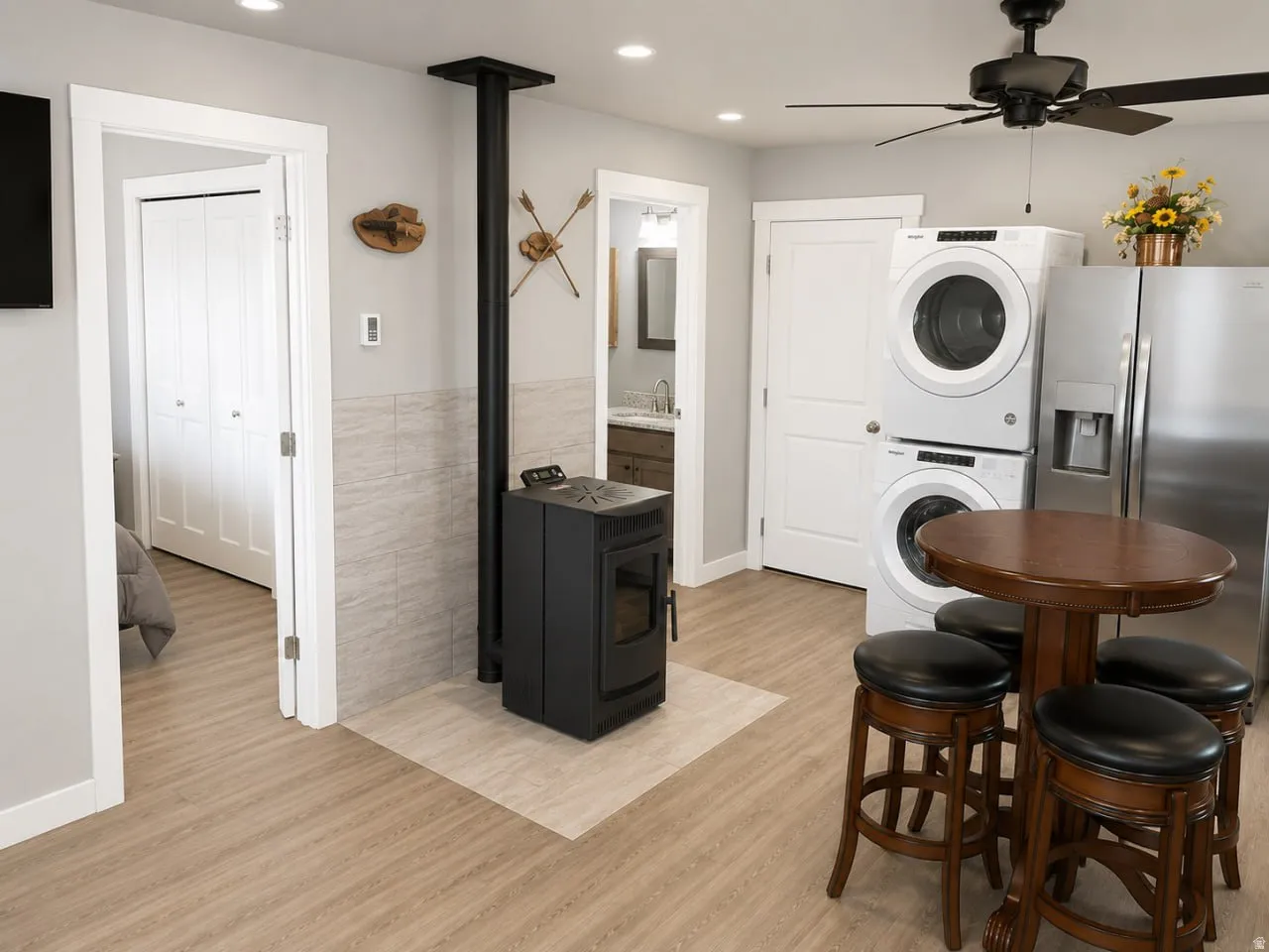 Interior featuring wood-finish flooring, a freestanding black stove, a full-size stainless steel refrigerator, and stacked laundry appliances