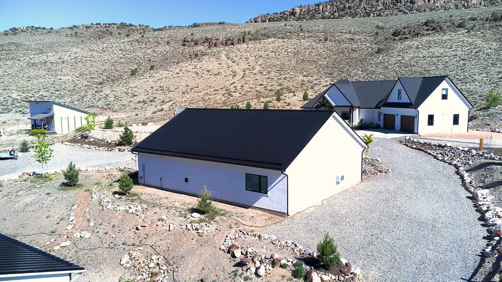 Expansive gravel driveway leading to a contemporary white dwelling with a black metal roof