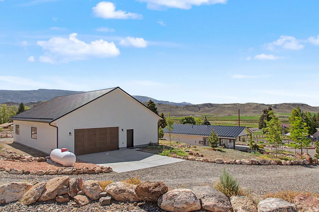 Modern farmhouse style home featuring white stucco siding, a black metal roof, and a two-car garage with wood-look doors