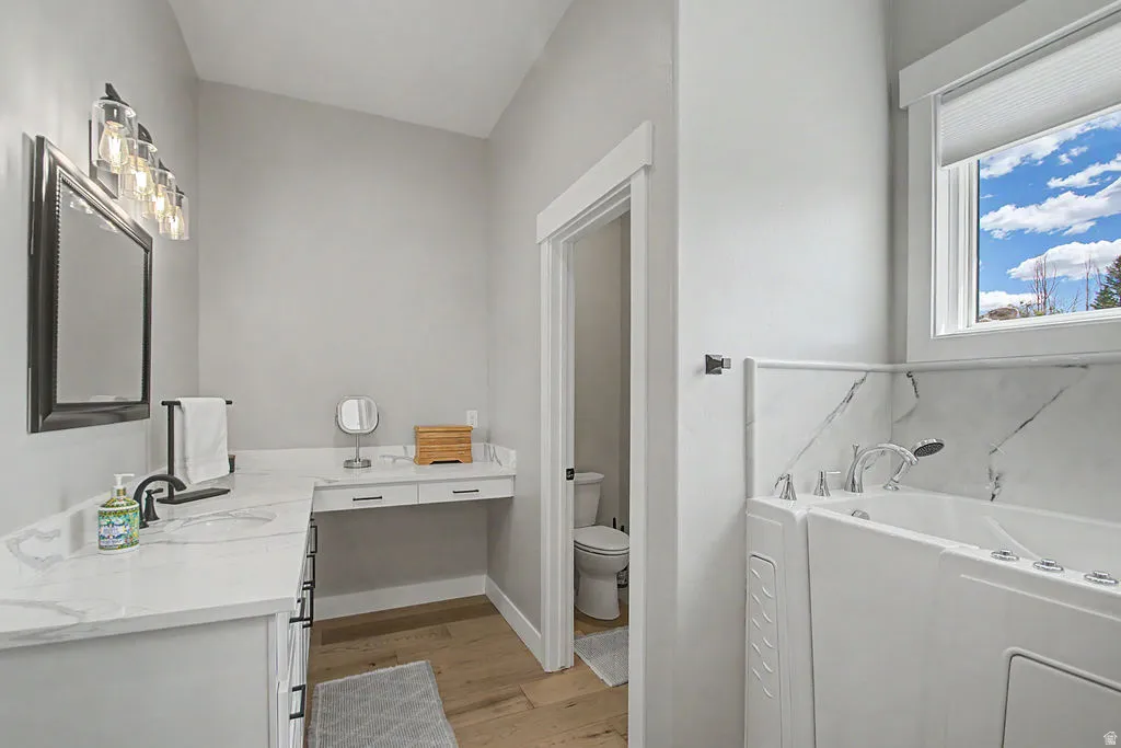Bathroom featuring a walk-in tub with chrome fixtures, a single vanity with a quartz-look countertop, dark bronze-finish hardware, a large framed mirror, and wood-finish flooring