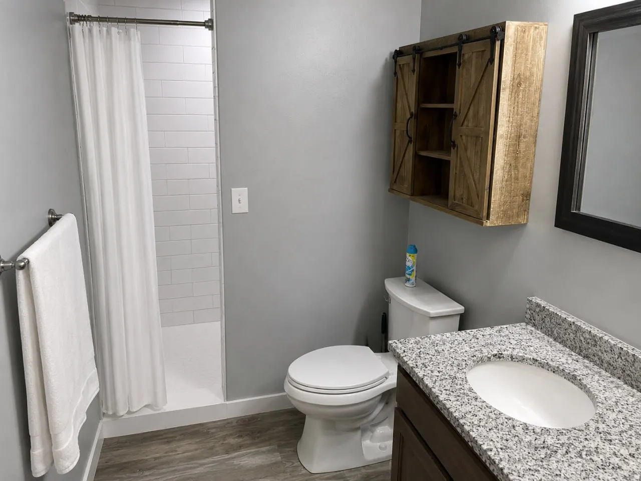 Full bathroom featuring a white subway tile shower, wood-finish flooring, and a vanity with a speckled countertop