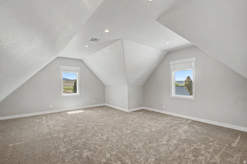 Bonus Room Spacious upper-level room featuring angled ceilings, recessed lighting, two windows with roller shades, and neutral carpet flooring