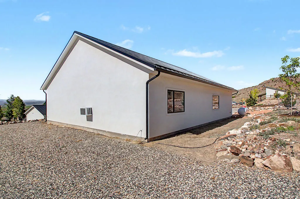 White stucco exterior with a dark asphalt shingle roof, black window frames, and a gravel ground cover