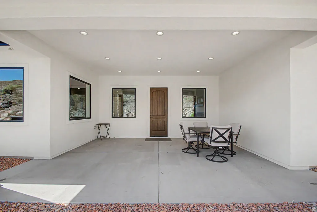 Expansive covered patio featuring a wood-panel entry door, recessed lighting, and surrounding desert landscaping