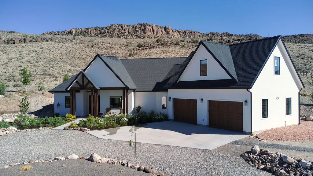 Contemporary residence featuring a white stucco exterior, dark shingle roof, two-car garage with wood-finish doors, and a covered entry with timber detailing