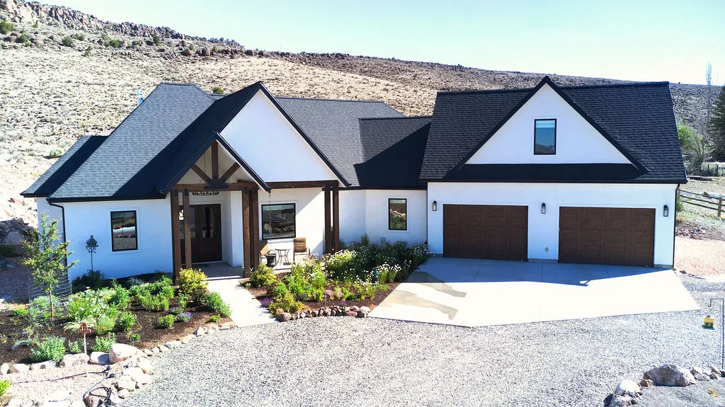 Modern farmhouse exterior featuring a white stucco finish, dark shingle roof, timber-frame entryway, and a dual-bay garage with wood-finish doors
