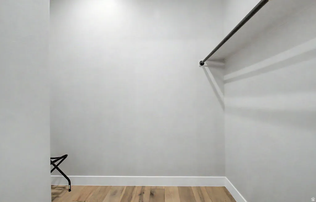 Recessed lighting illuminates a closet featuring a durable metal hanging rod and wood-finish flooring with white baseboards