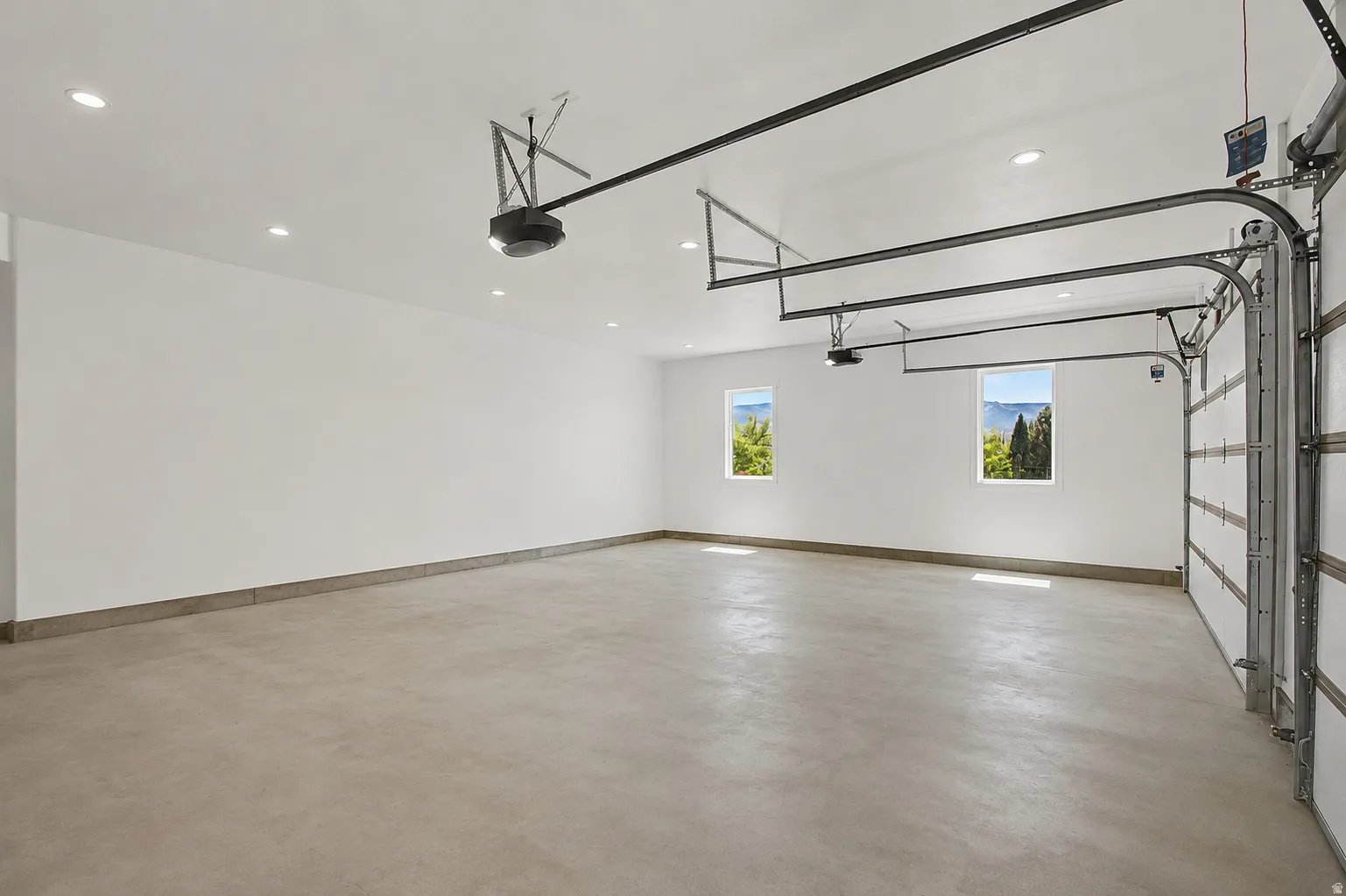 Spacious garage featuring a concrete floor, two windows providing natural light, recessed ceiling lighting, and exposed garage door mechanisms