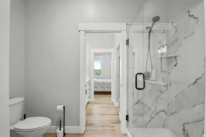 Modern bathroom featuring a glass-enclosed shower with quartz surround, a white toilet, and Hallmark Orris Maple   flooring