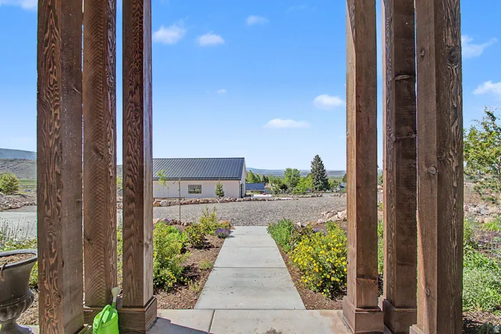 Expansive outdoor space featuring a concrete pathway, landscaped grounds with diverse plantings, and a distant building with a dark metal roof