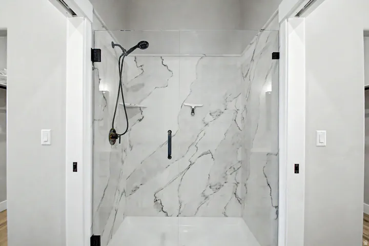 Walk-in shower featuring glass enclosure, quartz wall panels, matte black shower fixtures, and recessed lighting