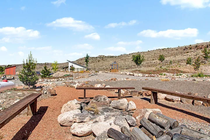 Outdoor gathering area featuring a rock-lined fire pit and multiple large wooden benches