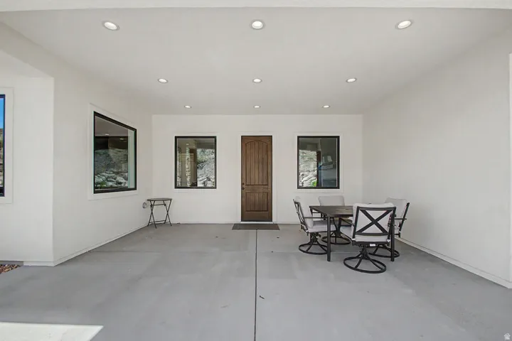 Covered patio with recessed lighting, a wood-finish entry door, and contemporary black-framed windows