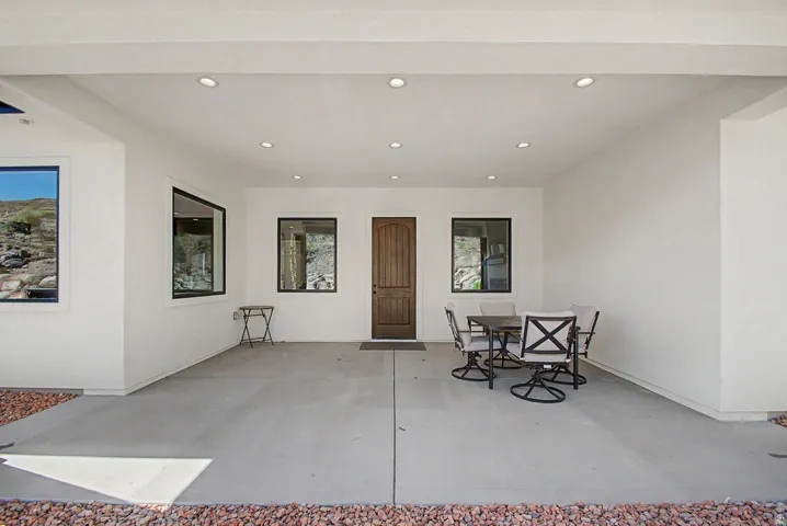 Expansive covered patio featuring a wood-panel entry door, recessed lighting, and surrounding desert landscaping