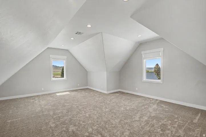 Bonus Room Spacious upper-level room featuring angled ceilings, recessed lighting, two windows with roman shades, and neutral carpet flooring