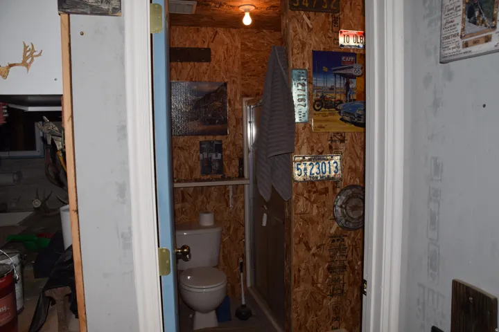 Compact bathroom featuring a white toilet, enclosed shower, and exposed wood-finish wall panels