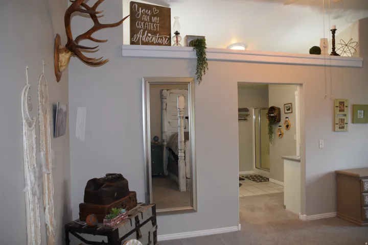 Carpeted room featuring a decorative shelf, an open doorway, and a full-length mirror