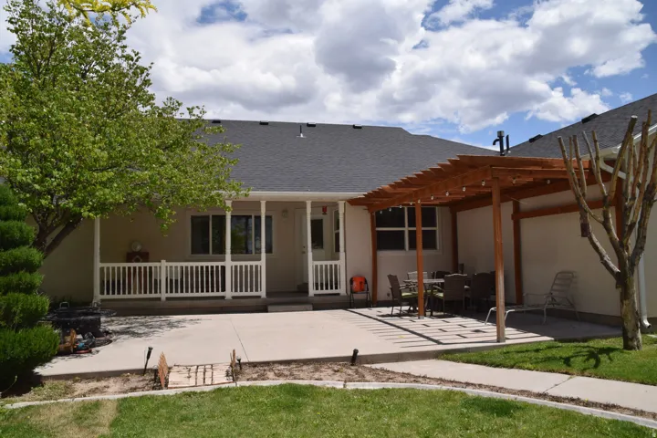 Expansive concrete patio featuring a wood pergola, a covered porch with white railing, and a manicured lawn area