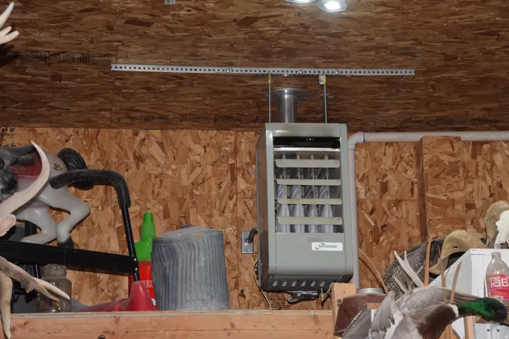 Wall-mounted heating unit with visible ducting, installed against an oriented strand board wall and ceiling