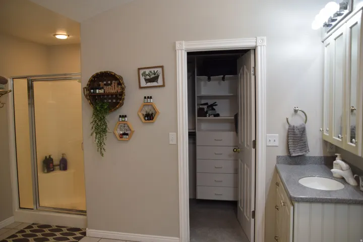 Bathroom featuring a sliding glass shower enclosure, a vanity with an undermount sink and a speckled countertop, white cabinetry, and a walk-in closet with built-in shelving and drawers