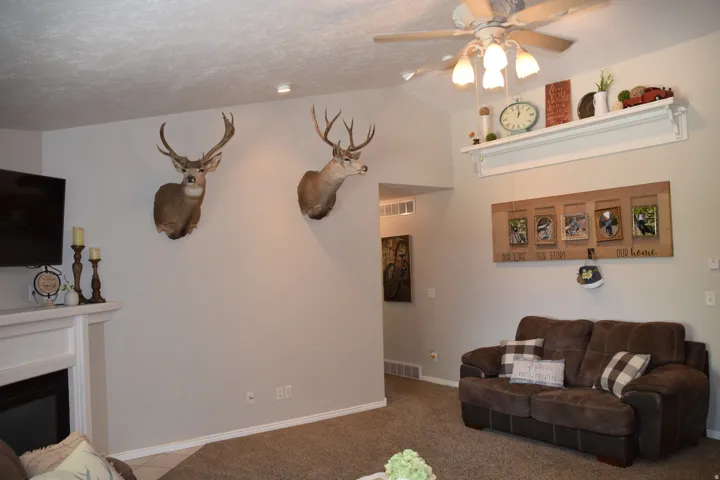 Living area featuring a vaulted ceiling with a ceiling fan, a built-in fireplace with a white mantel, and light-toned walls