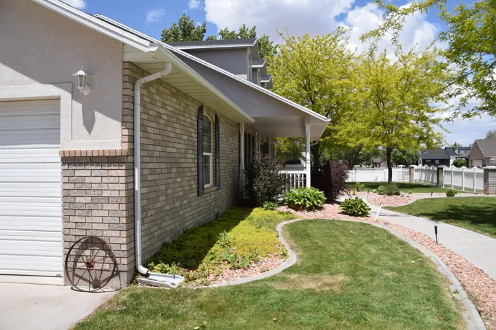 Exterior featuring a brick and stucco facade, an integrated garage, a covered front porch, a concrete walkway, and landscaped garden beds with mature trees